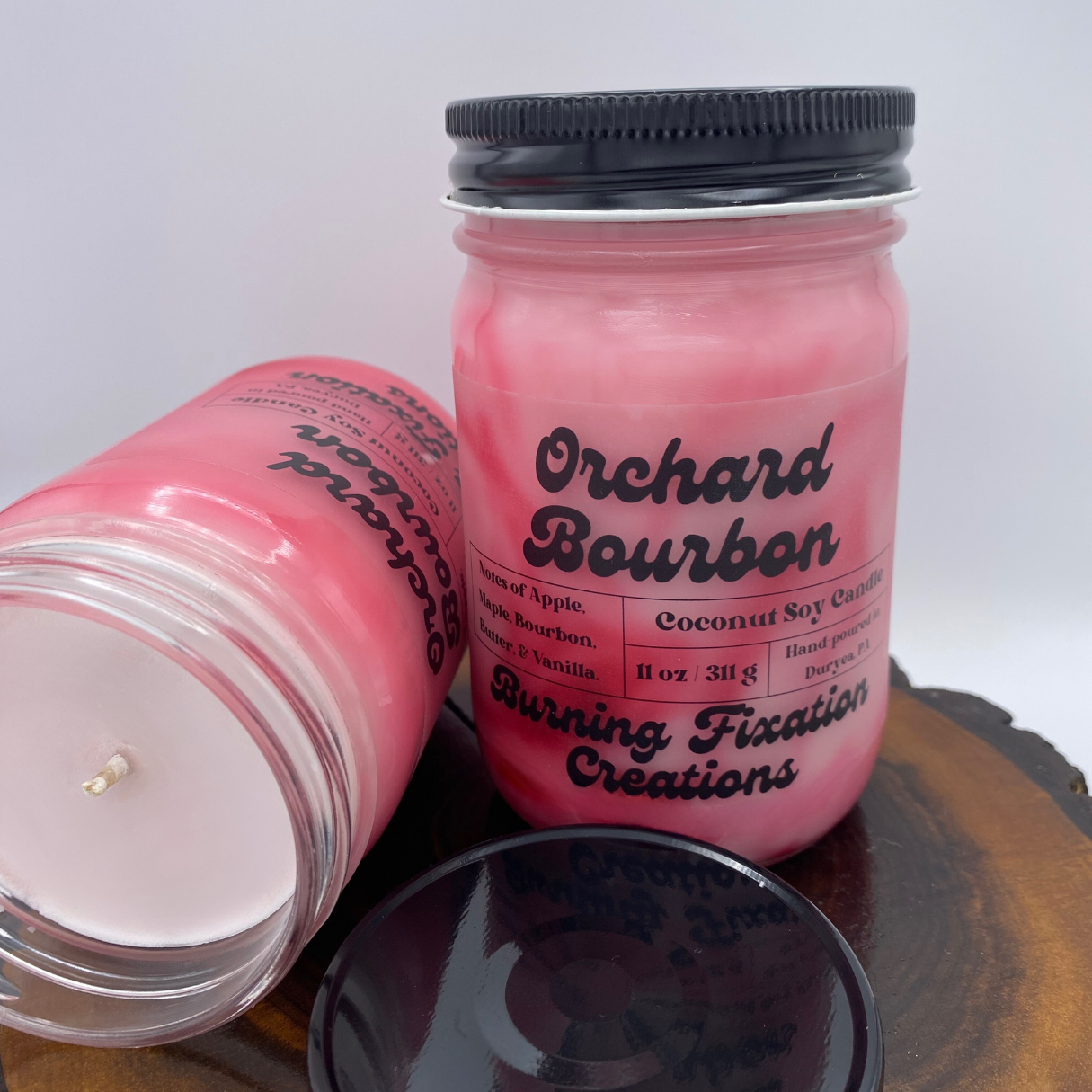 two coconut soy candles in glass jars with black lids Scent: Orchard Bourbon, Color: Red, pink, white swirled